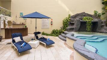 A poolside area with lounge chairs, a blue umbrella, a small bar, and a decorative rock wall.