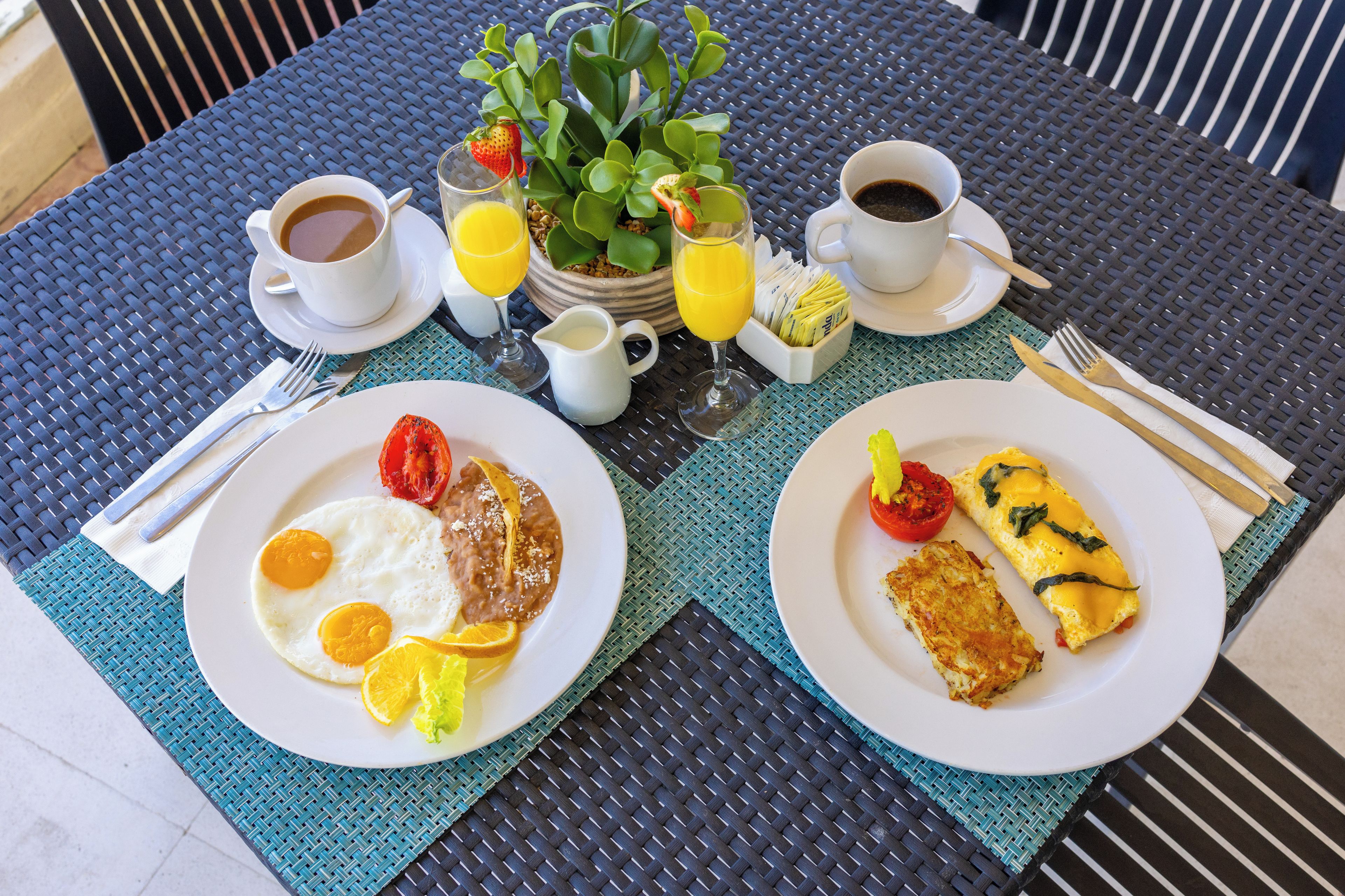 A breakfast setting with two plates of food, a coffee cup, a glass of orange juice, and a small plant on a table.