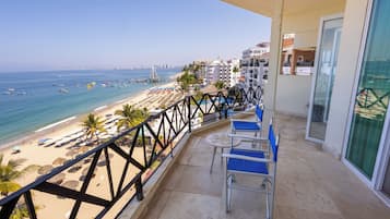 A balcony with a view of a beach, a railing, and a table with chairs.