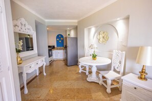 A dining area with a white table and chairs, a white console table with a lamp, and a kitchen in the background.