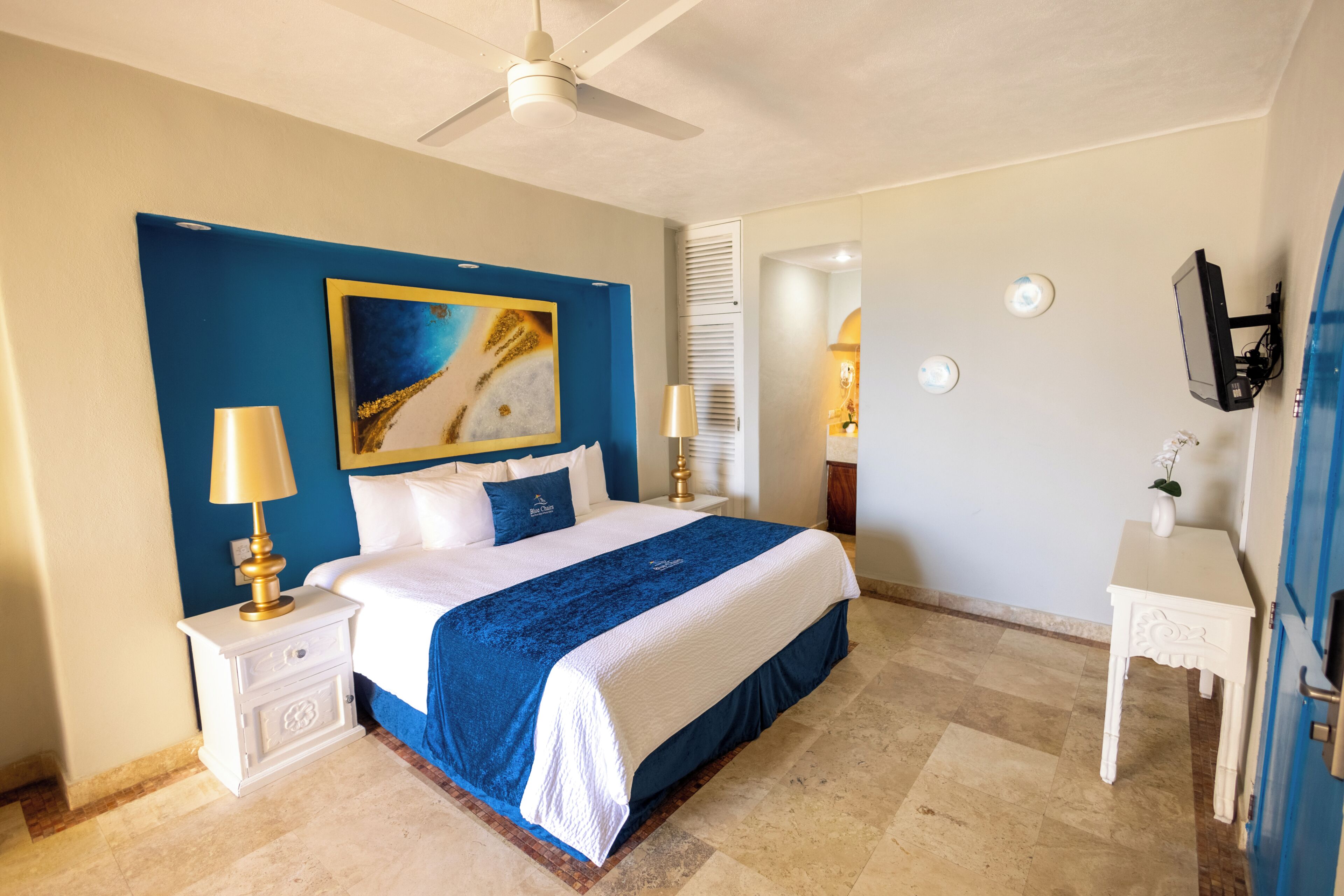 A hotel room with a bed, nightstand, lamp, painting, and a TV on a stand.