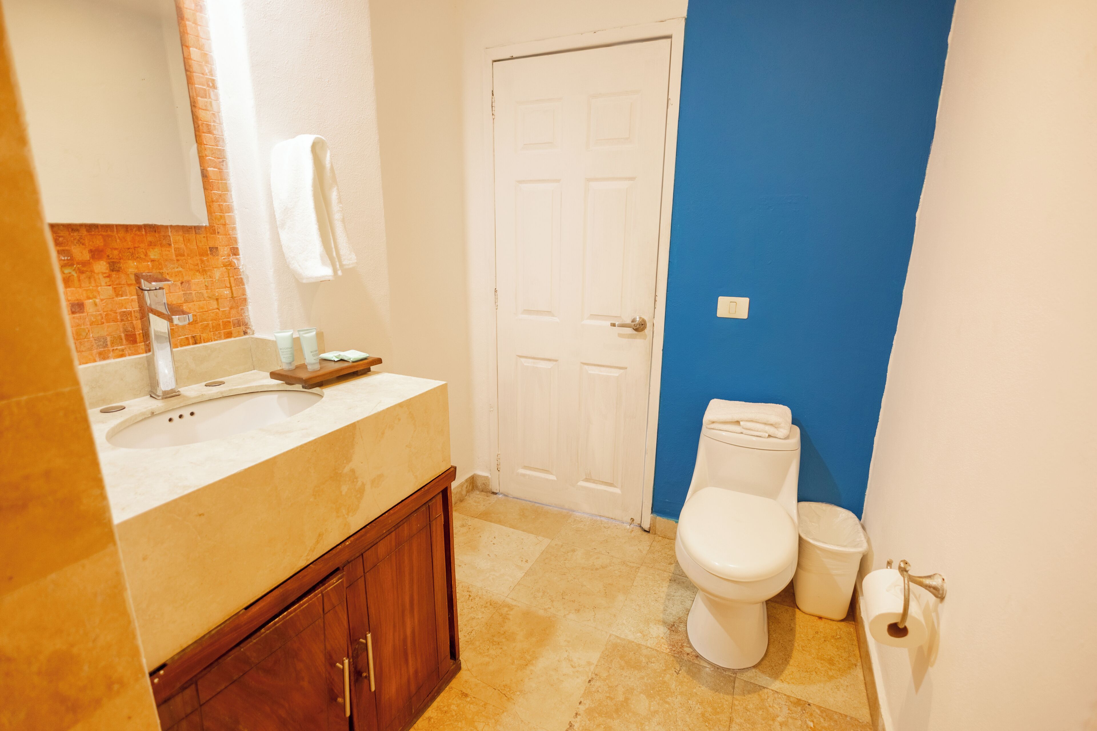 Un baño con lavamanos, espejo, toallero, inodoro y pared azul.