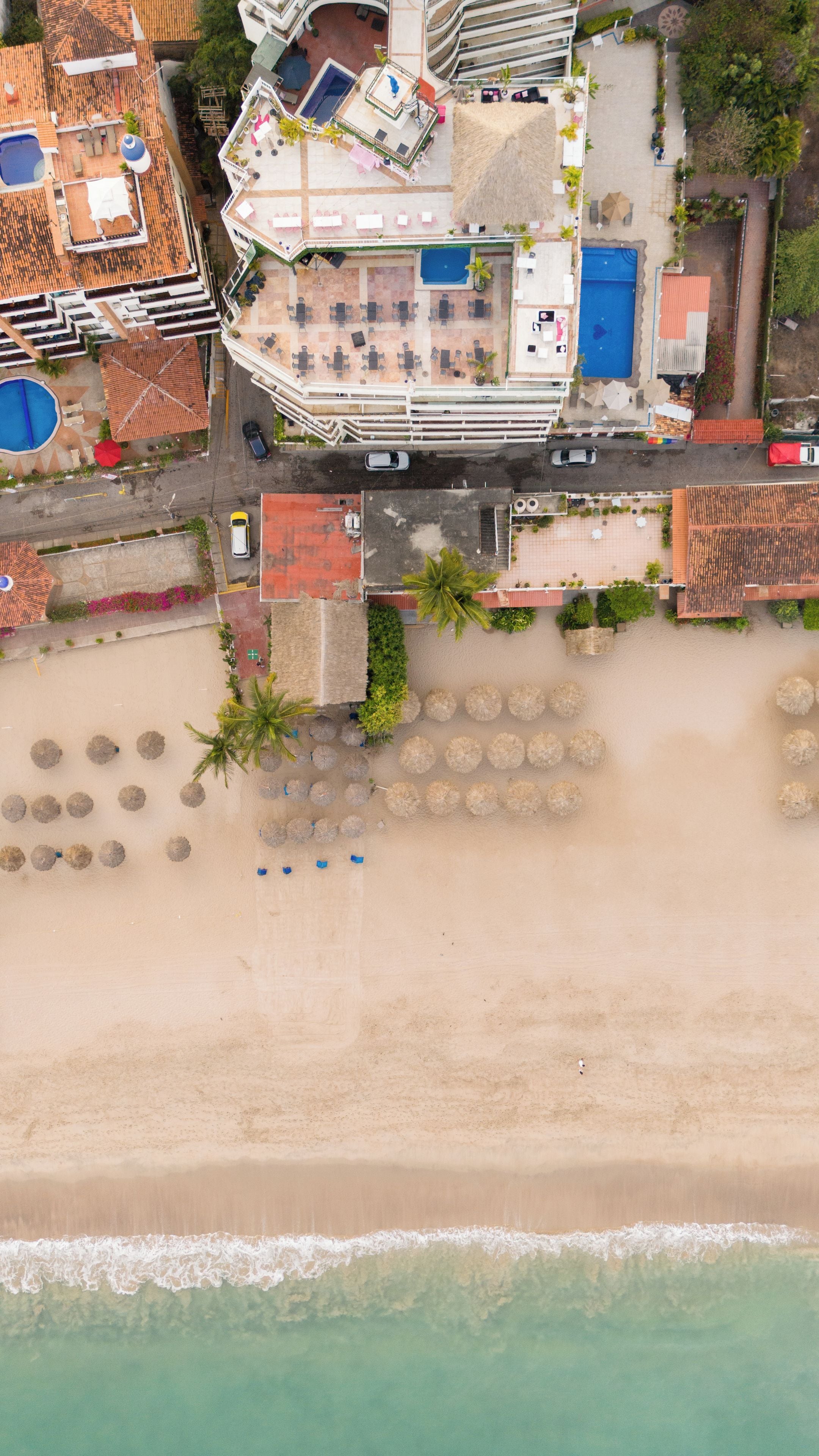 Vista aérea de un complejo turístico con piscina, sombrillas de playa y una zona de playa.