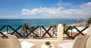 A balcony with a view of the beach, palm trees, and a distant city skyline. - Blue Chairs Beachfront Resort Puerto Vallarta Mexico - Adults Only (Puerto Vallarta)