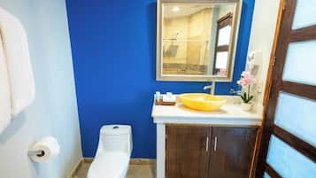 Een badkamer met een blauwe wand, een wit toilet, een geel wastafelmeubel en een spiegel boven het wastafelmeubel.