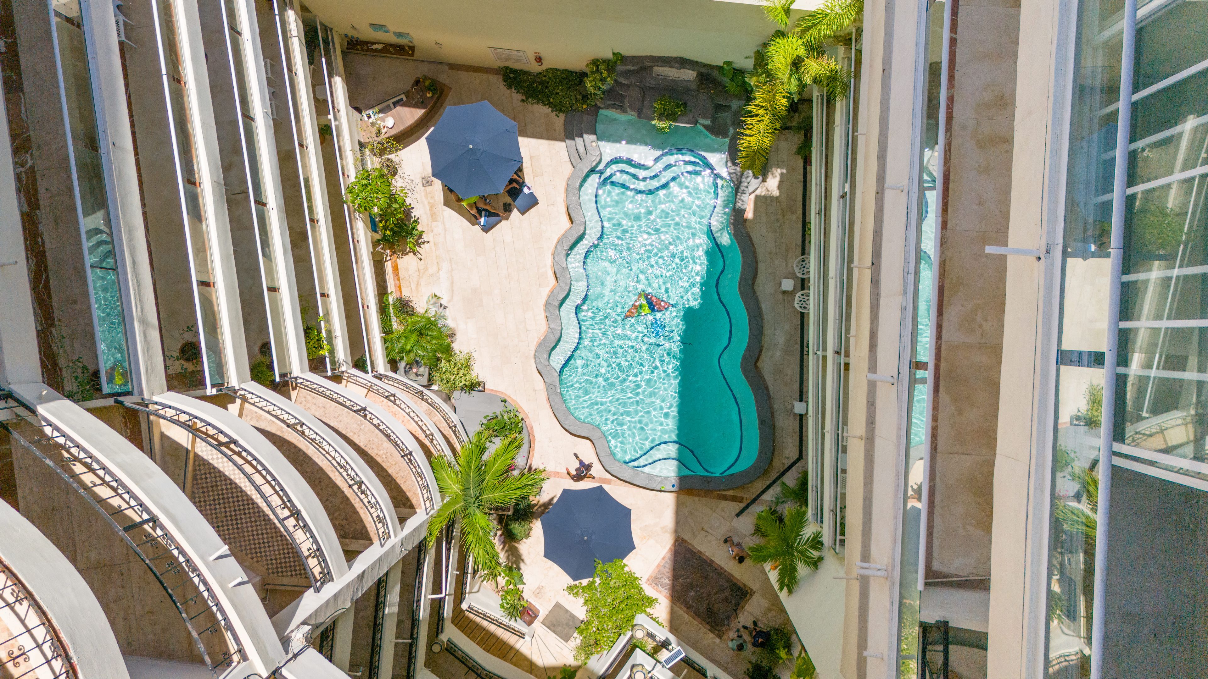 Vista aérea de un hotel con piscina rodeada de palmeras y mobiliario para exteriores.