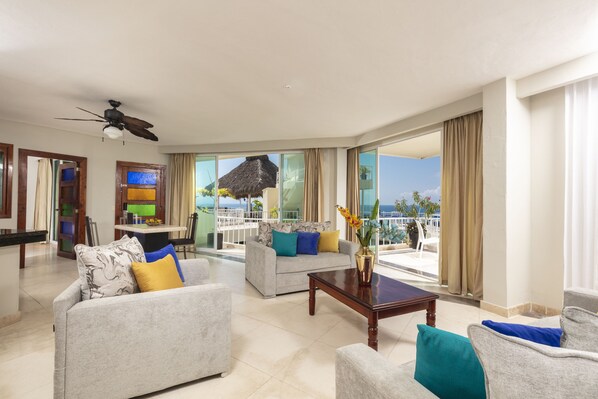 A spacious living area with a ceiling fan, two sofas with colorful cushions, a wooden coffee table, and a large window offering a view of the ocean. - Blue Chairs Beachfront Resort Puerto Vallarta Mexico - Adults Only (Puerto Vallarta)