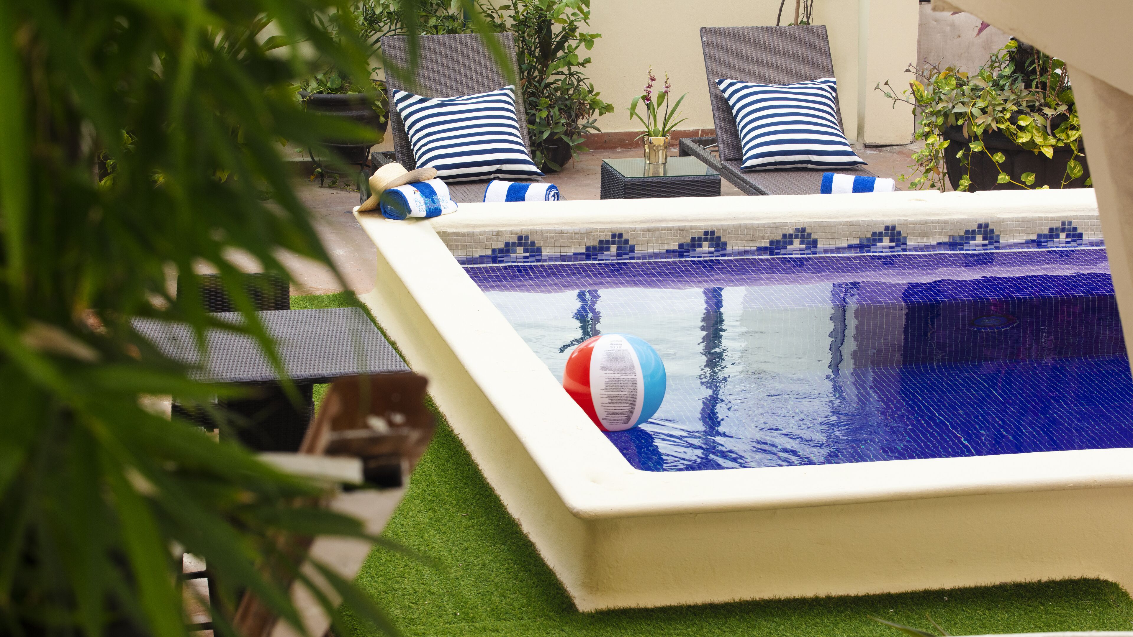 Una piscina con borde de azulejos azules, rodeada de sillones y almohadones a rayas.