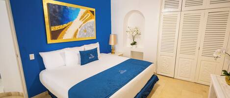 A hotel room with a bed, a painting, a lamp, a vase with flowers, and a wardrobe.