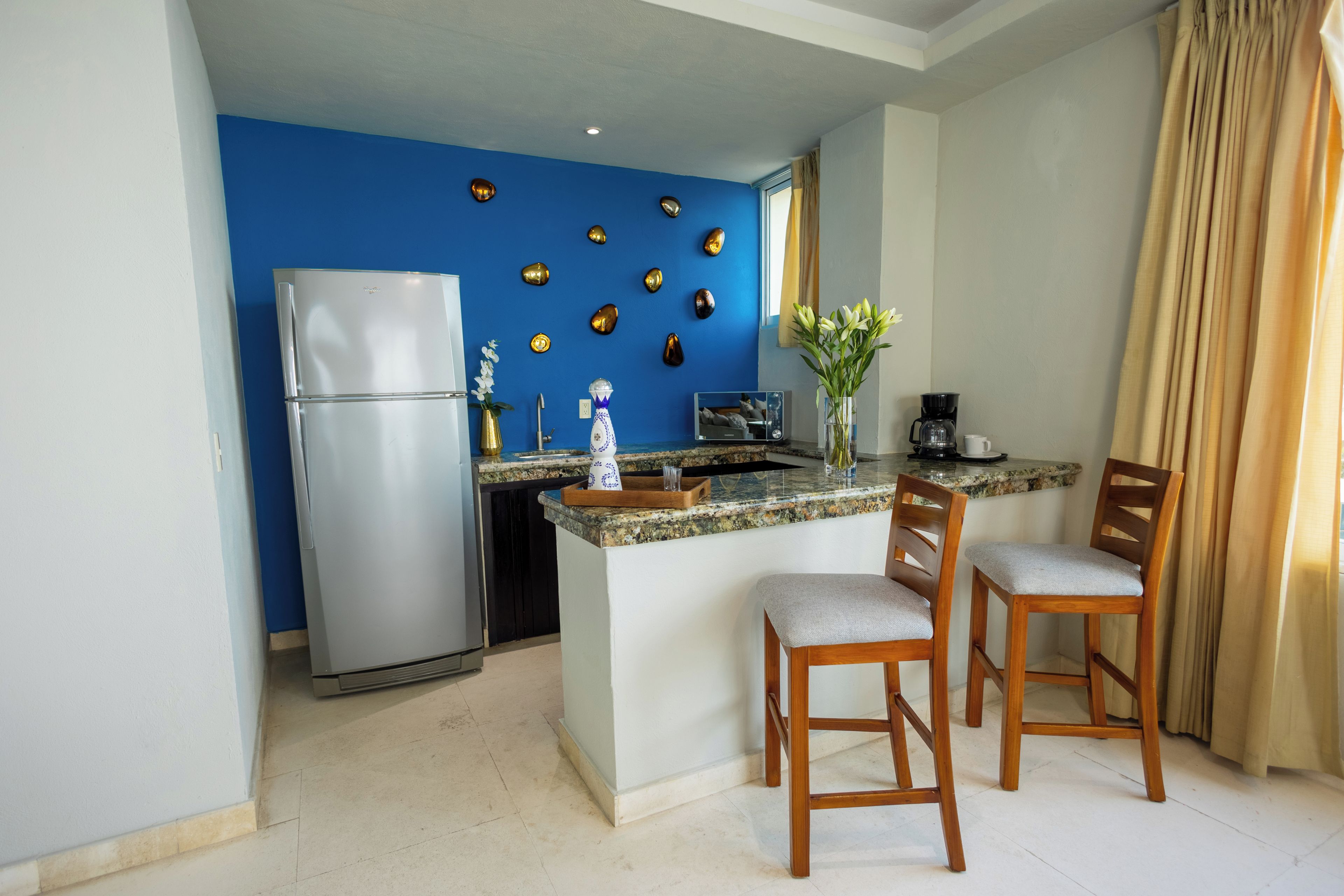 A compact kitchen with a refrigerator, a coffee maker, and a small island with two chairs.