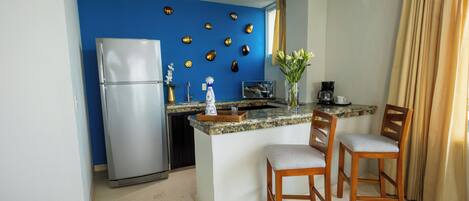 A compact kitchen with a refrigerator, a coffee maker, and a small island with two chairs.