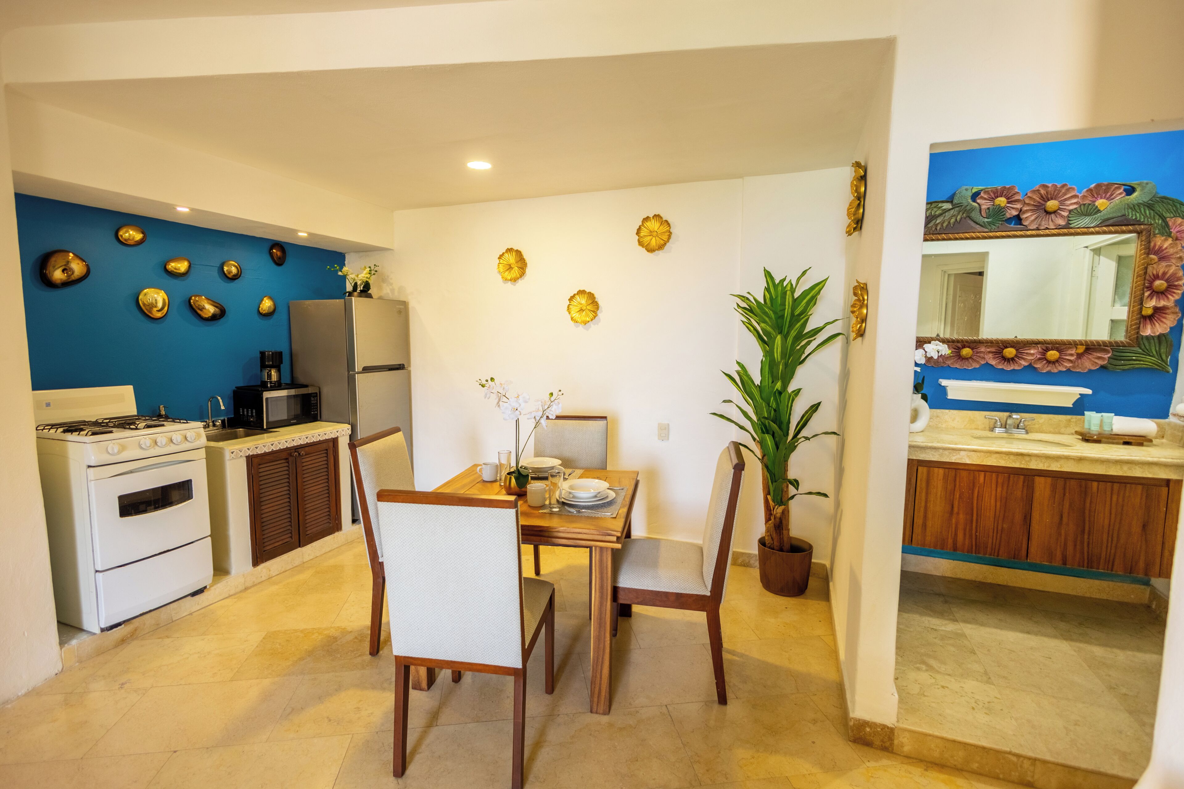 Una cucina funzionale con fornelli, microonde e frigorifero, una zona pranzo con tavolo e sedie, e un bagno con lavandino e specchio.