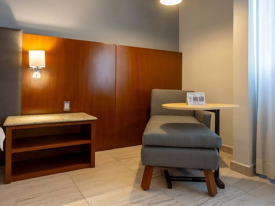 A hotel room with a bed, a wooden headboard, a small table, and a chair.