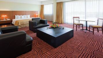 A hotel room with a bed, two sofas, a coffee table with fruit, a desk, and a chair.