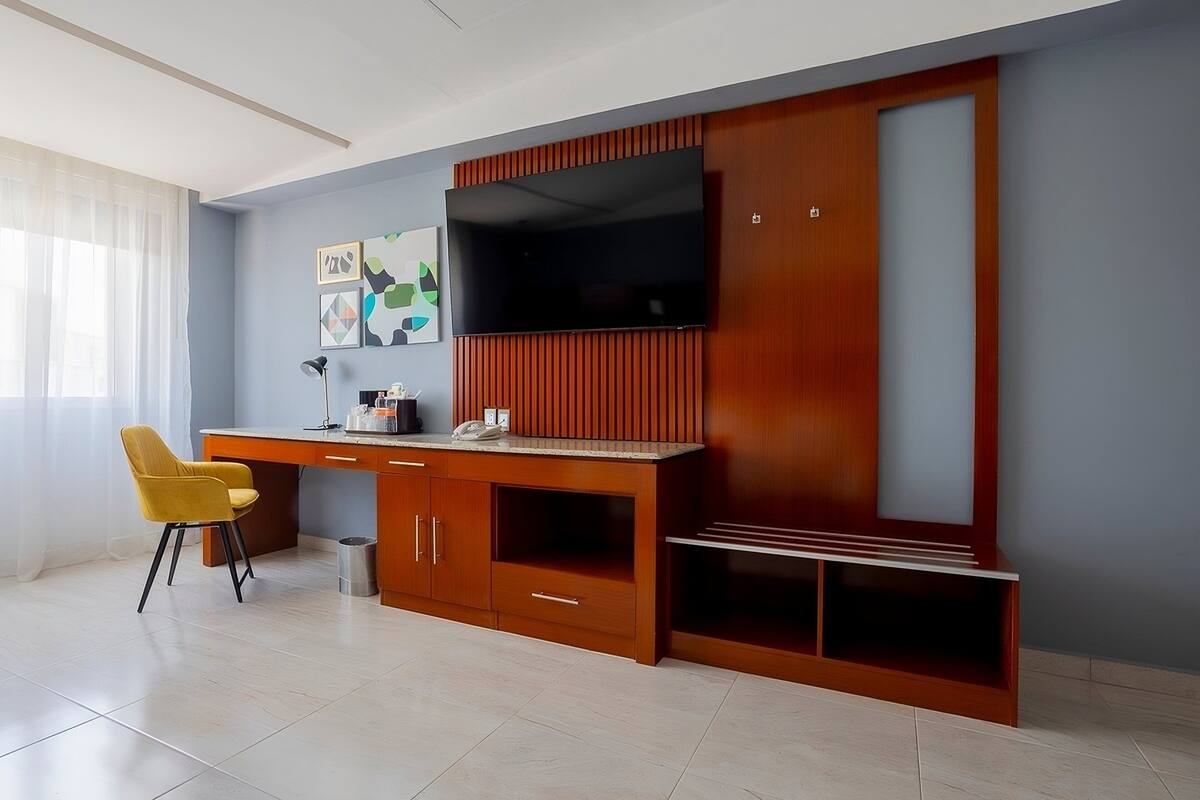 A modern living room with a wooden entertainment unit, a flat-screen TV, a yellow chair, and a desk.