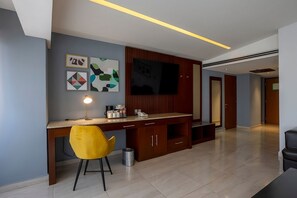 A modern living room with a wooden desk, a yellow chair, a TV mounted on the wall, and artwork. - Holiday Inn Puebla Finsa by IHG (Puebla)