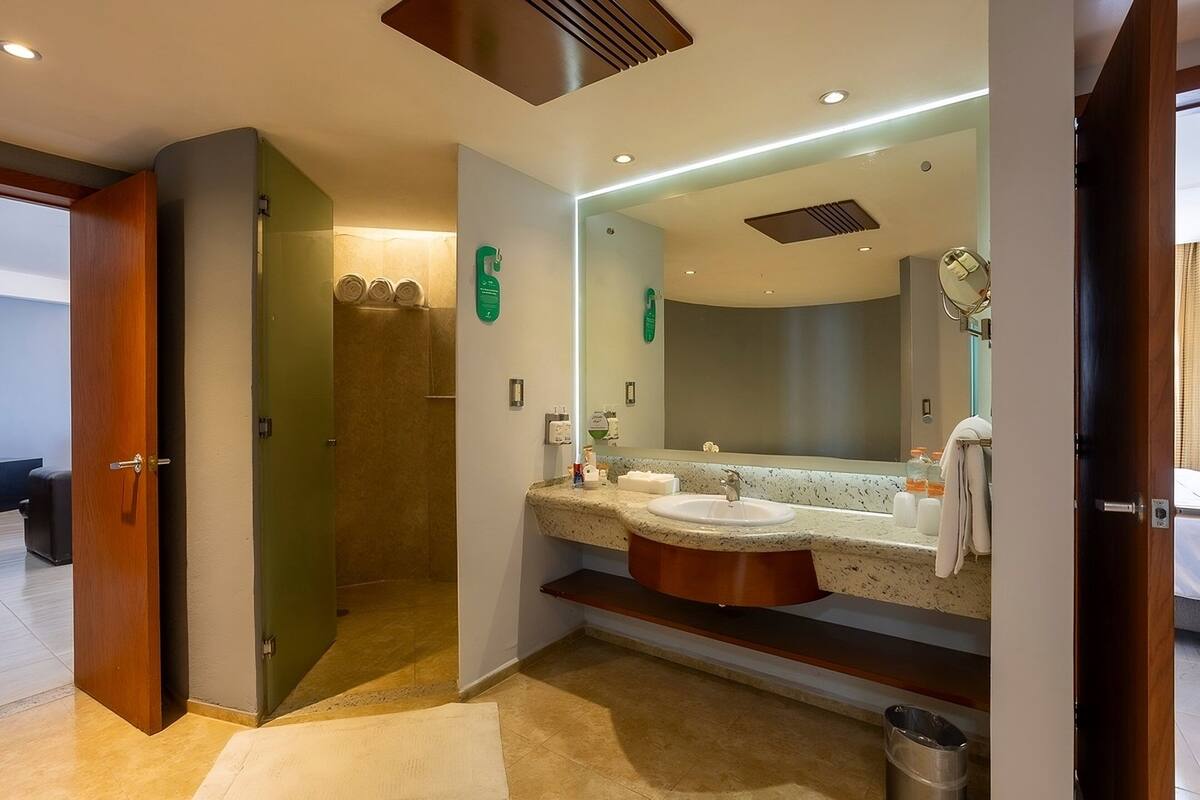 A modern bathroom with a large mirror, two sinks, and a shower area.