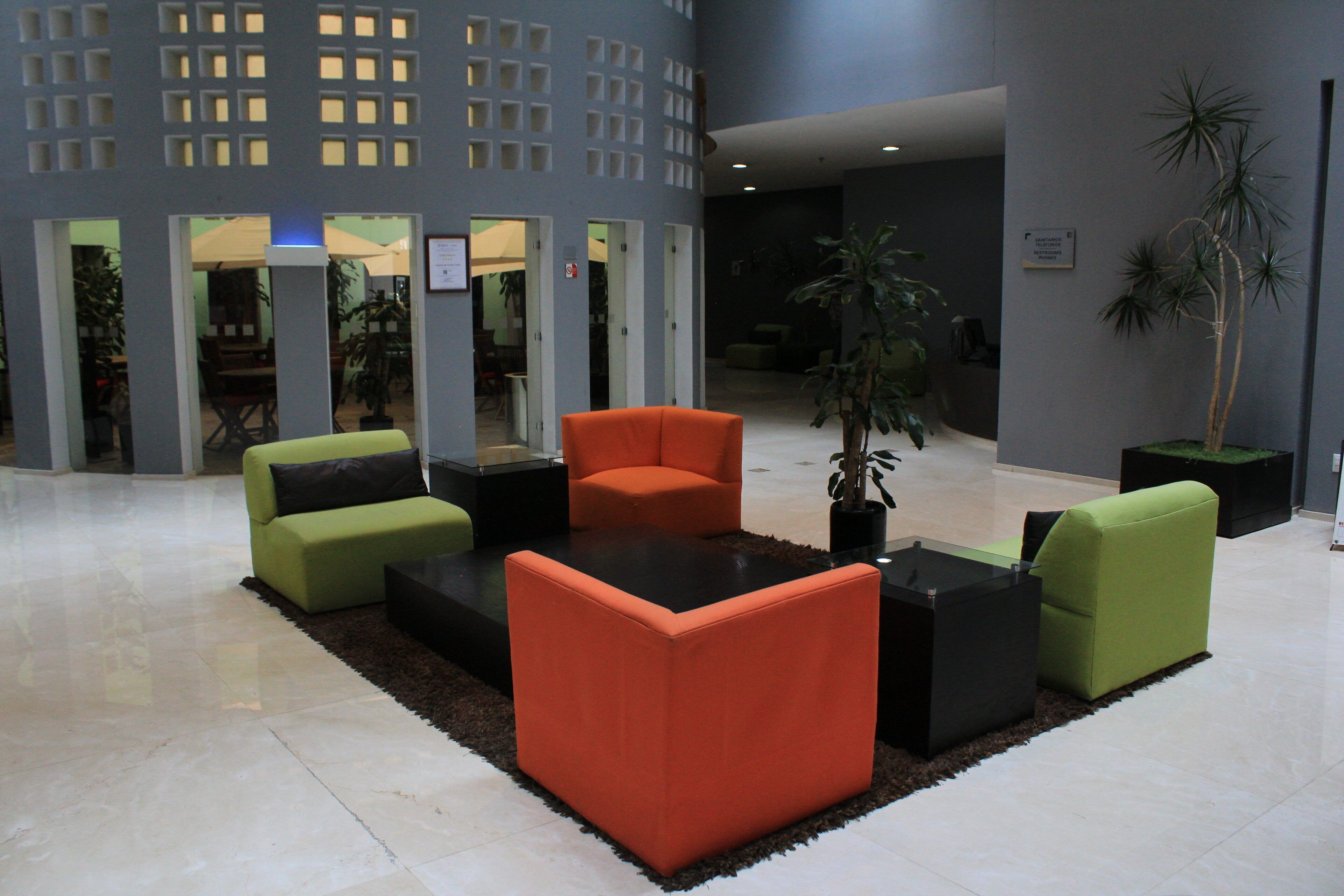 Un hall d’entrée doté d’un mobilier moderne, comprenant des canapés orange et verts, des tables basses noires et une plante en pot.