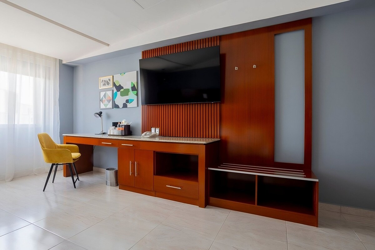 A modern living room with a wooden entertainment unit, a flat-screen TV, a yellow chair, and a desk.