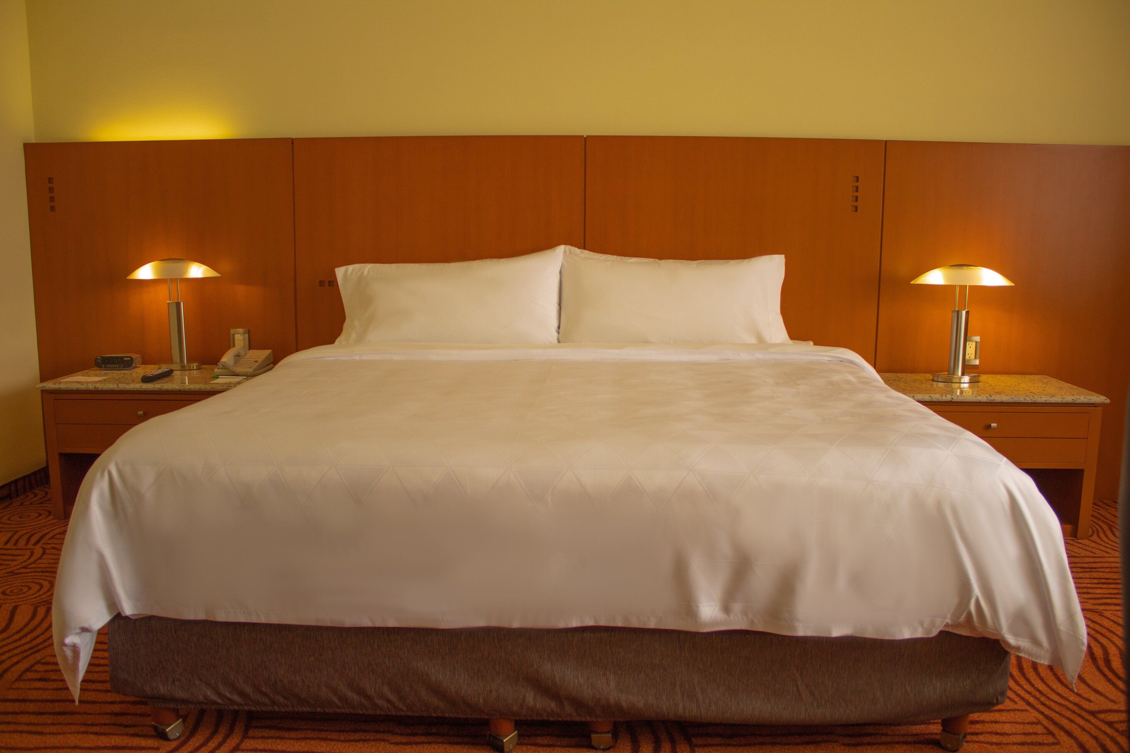 A hotel room with a large bed, two bedside tables with lamps, and a carpeted floor.