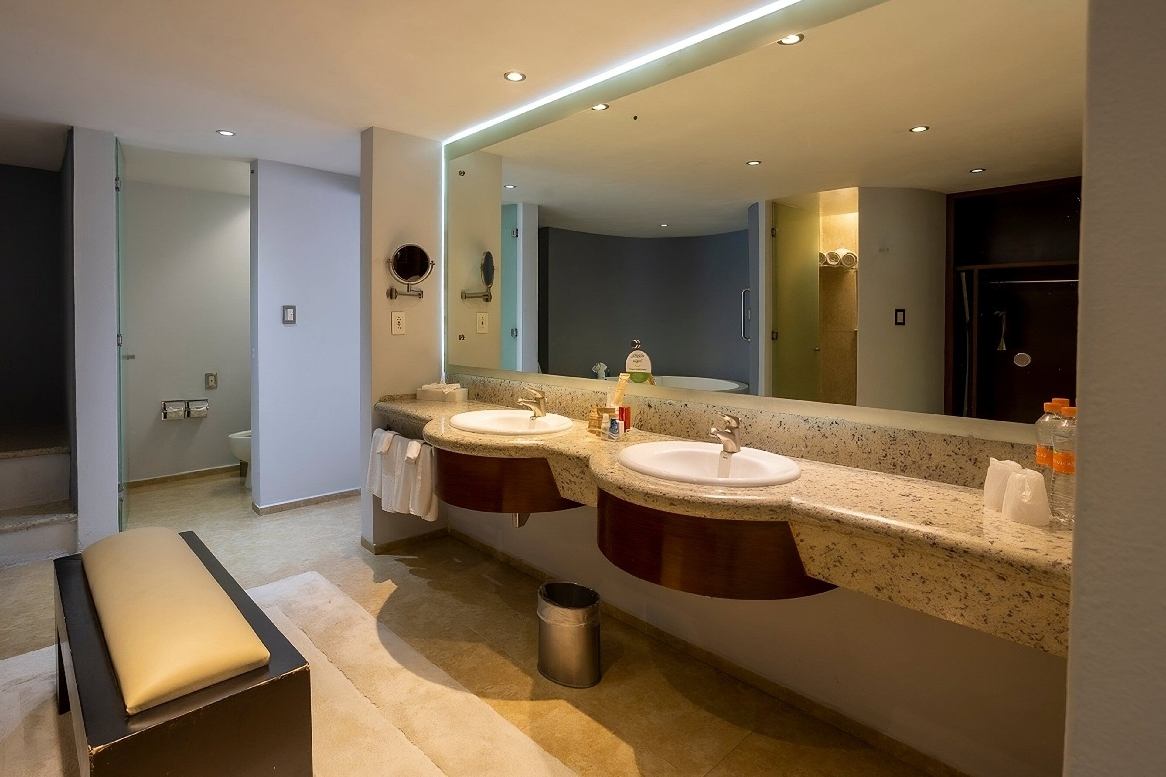 A modern bathroom with two sinks, a large mirror, and a bench.