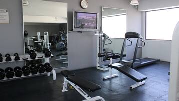 Un gimnasio con equipo de ejercicio, una banca, mancuernas, una cinta de correr y un televisor.