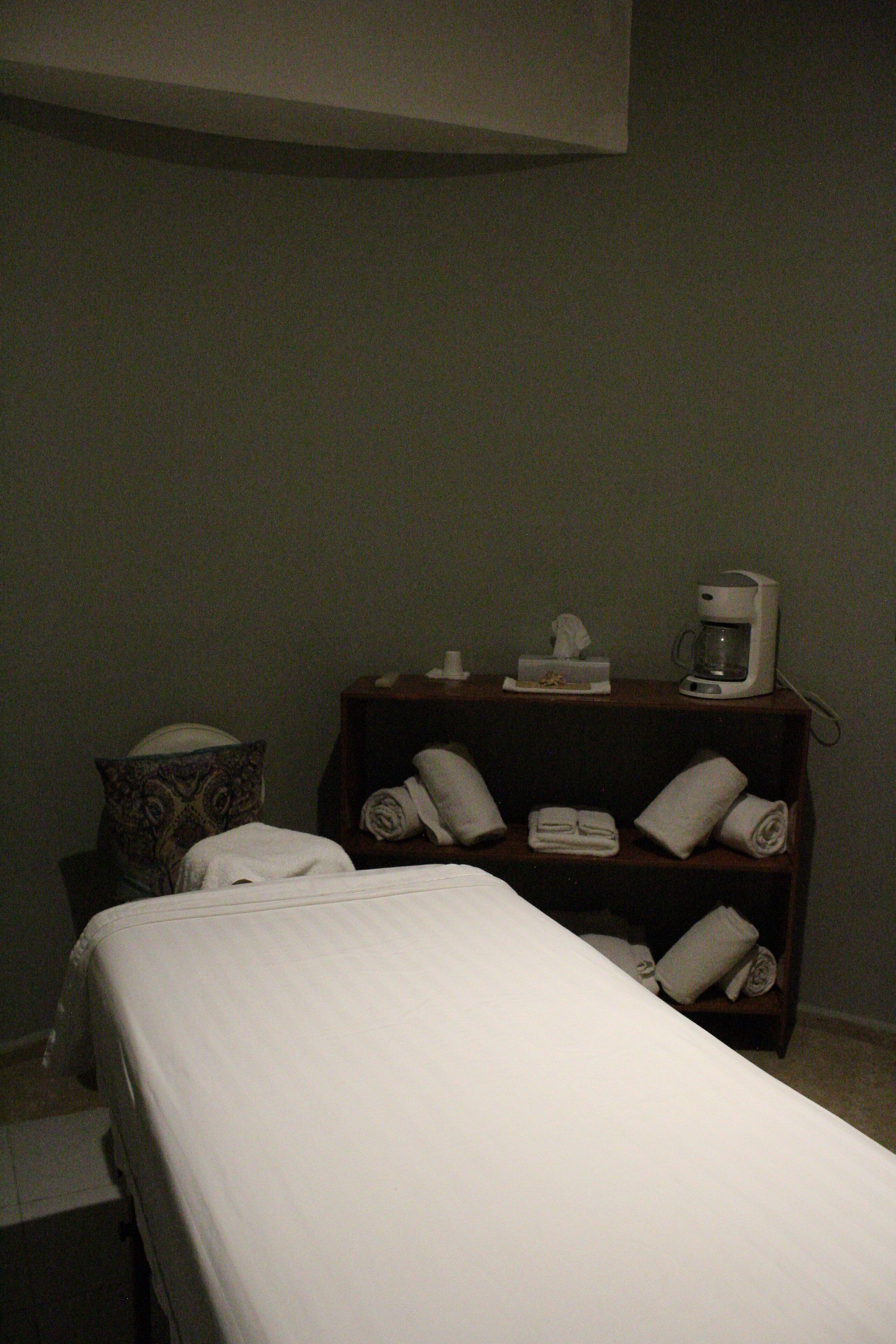 A hotel room with a bed, a bedside table with a coffee maker, and a shelf with towels.