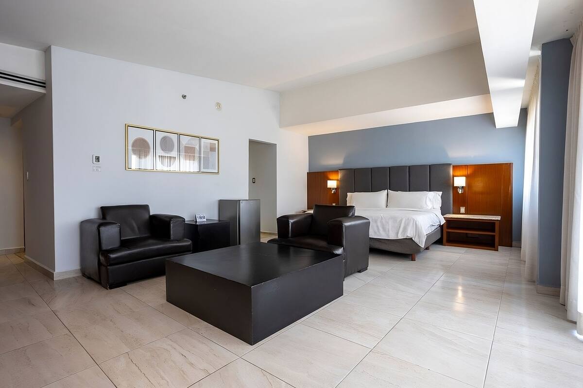 A modern hotel room with a bed, two sofas, a coffee table, and a nightstand.
