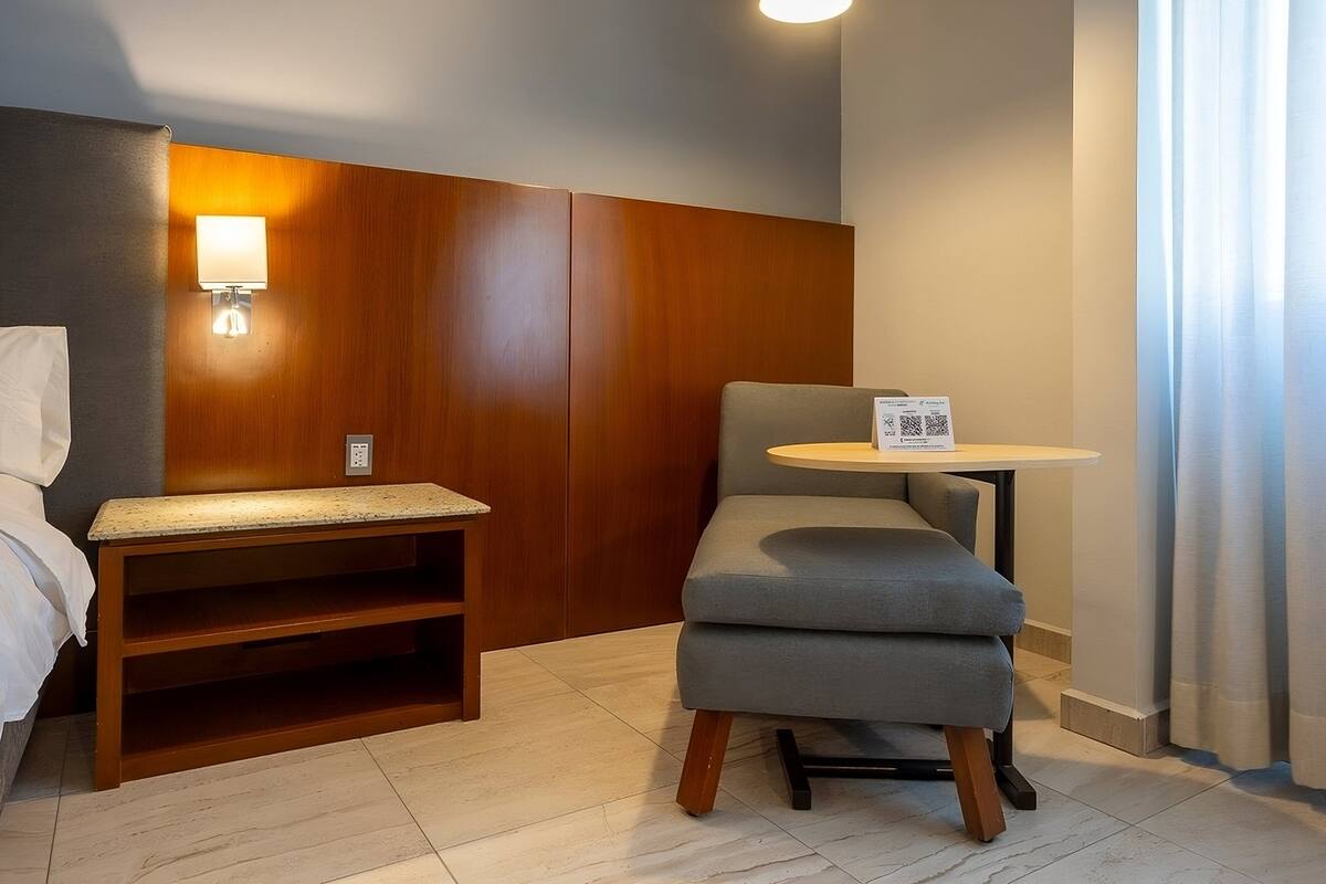 A hotel room with a bed, a wooden headboard, a small table, and a chair.