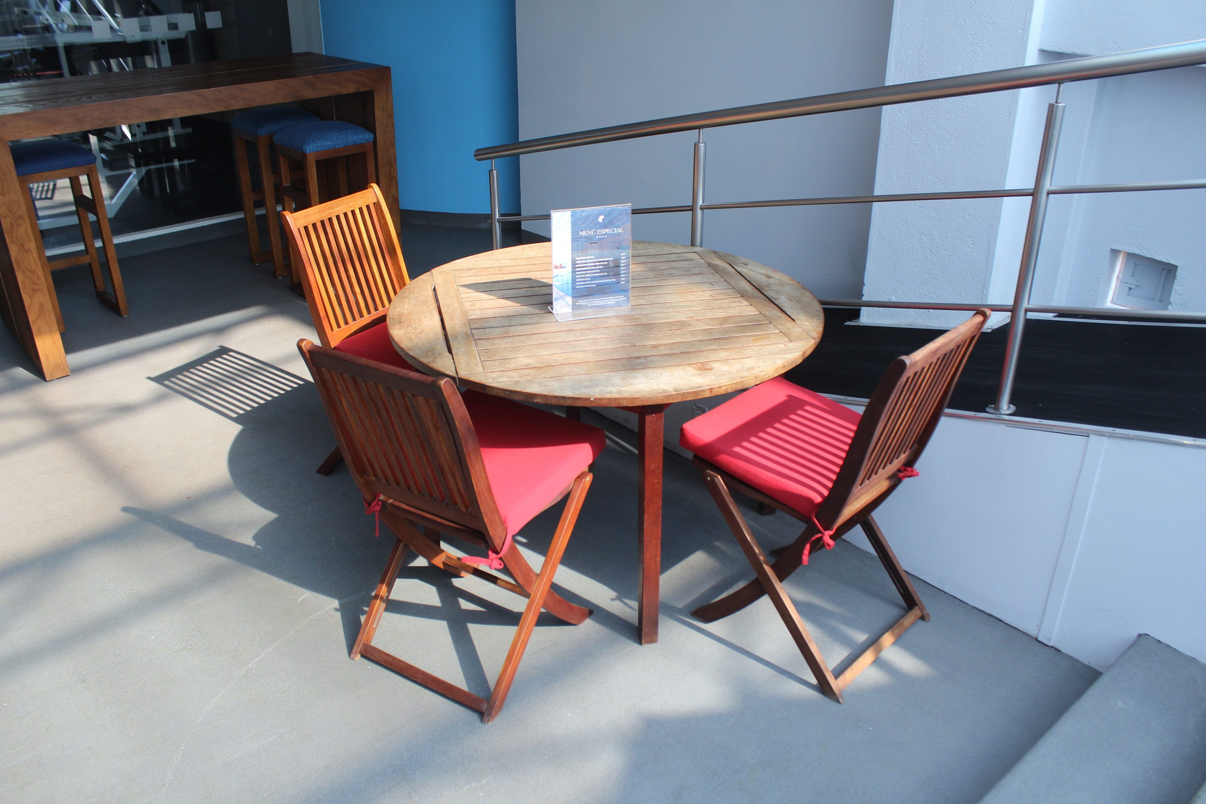 A round wooden table with four chairs, a menu stand, and a metal railing.
