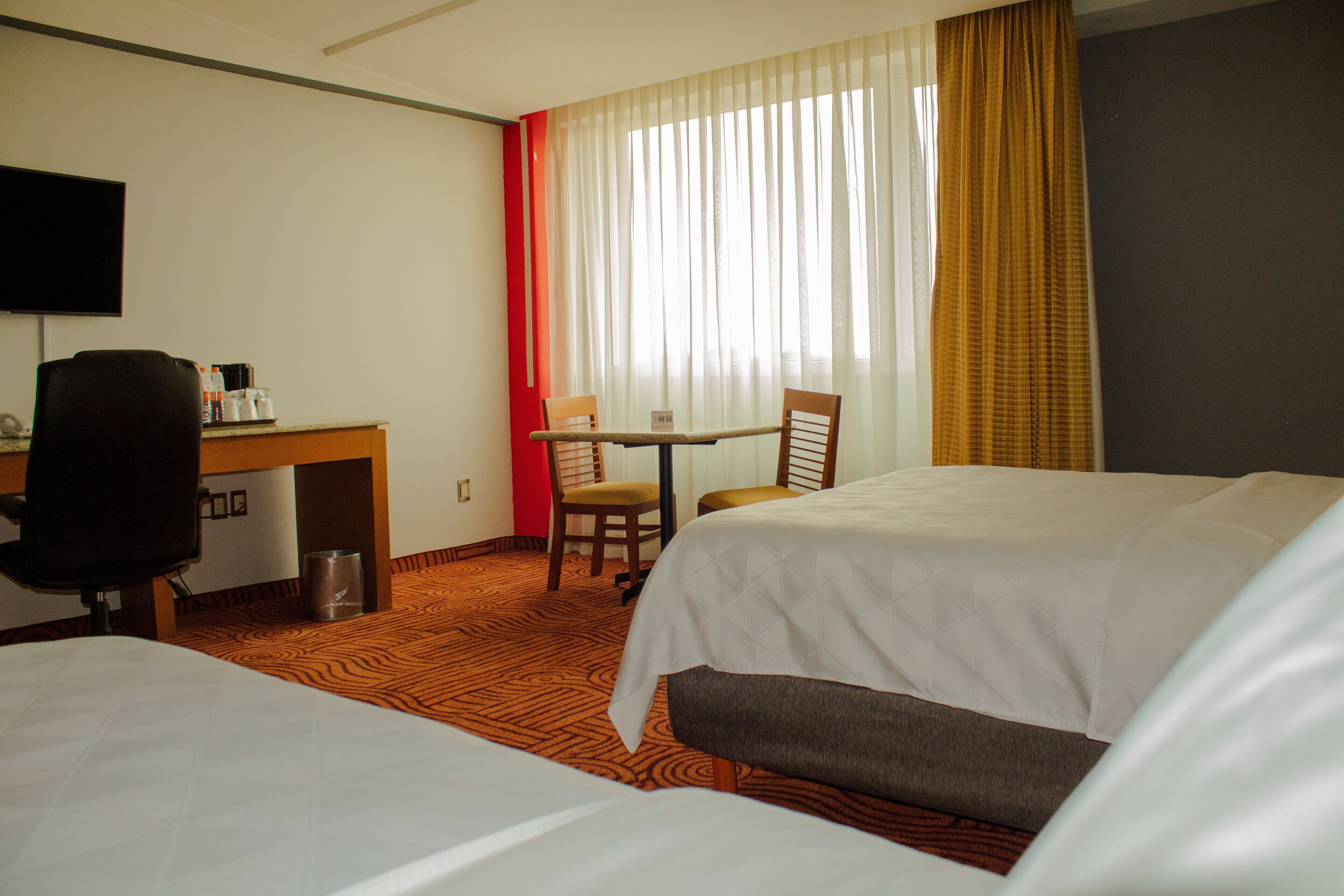 A hotel room with two beds, a desk, a chair, a television, and a window with curtains.