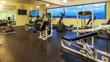 Ein Fitnessraum mit unterschiedlichen Trainingsgeräten, einem großen Fenster mit Blick und einer Uhr an der Wand.