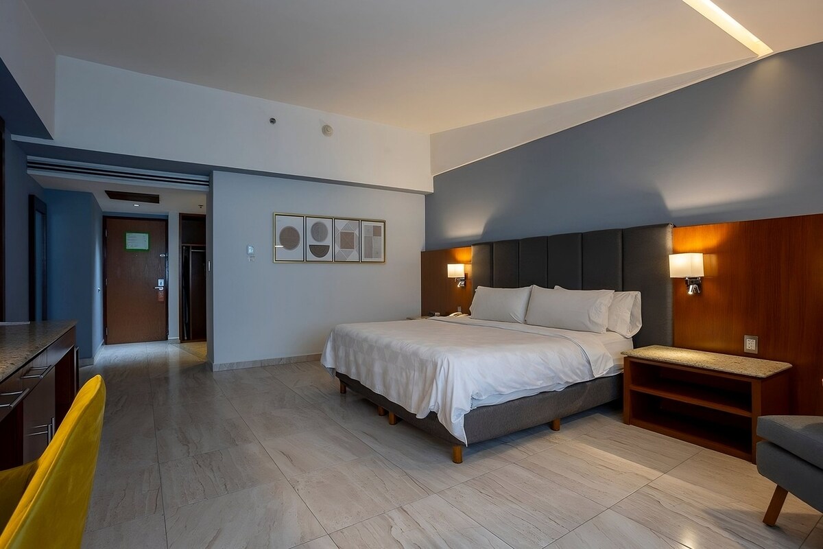 A modern hotel room with a bed, bedside tables, a desk, and a chair.