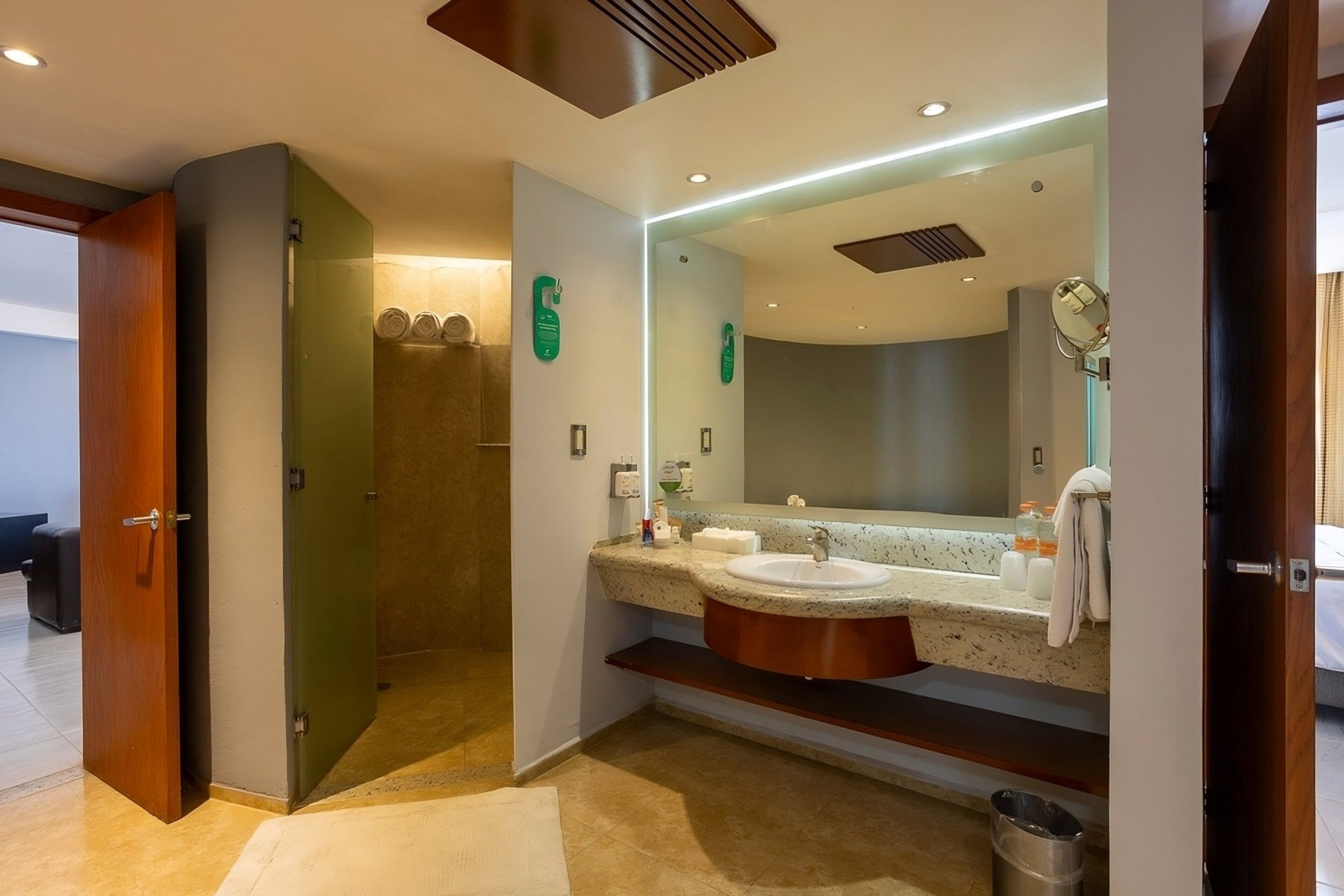 A modern bathroom with a large mirror, two sinks, and a shower area.