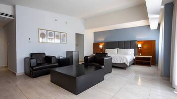 A modern hotel room with a bed, two armchairs, a coffee table, and a desk.