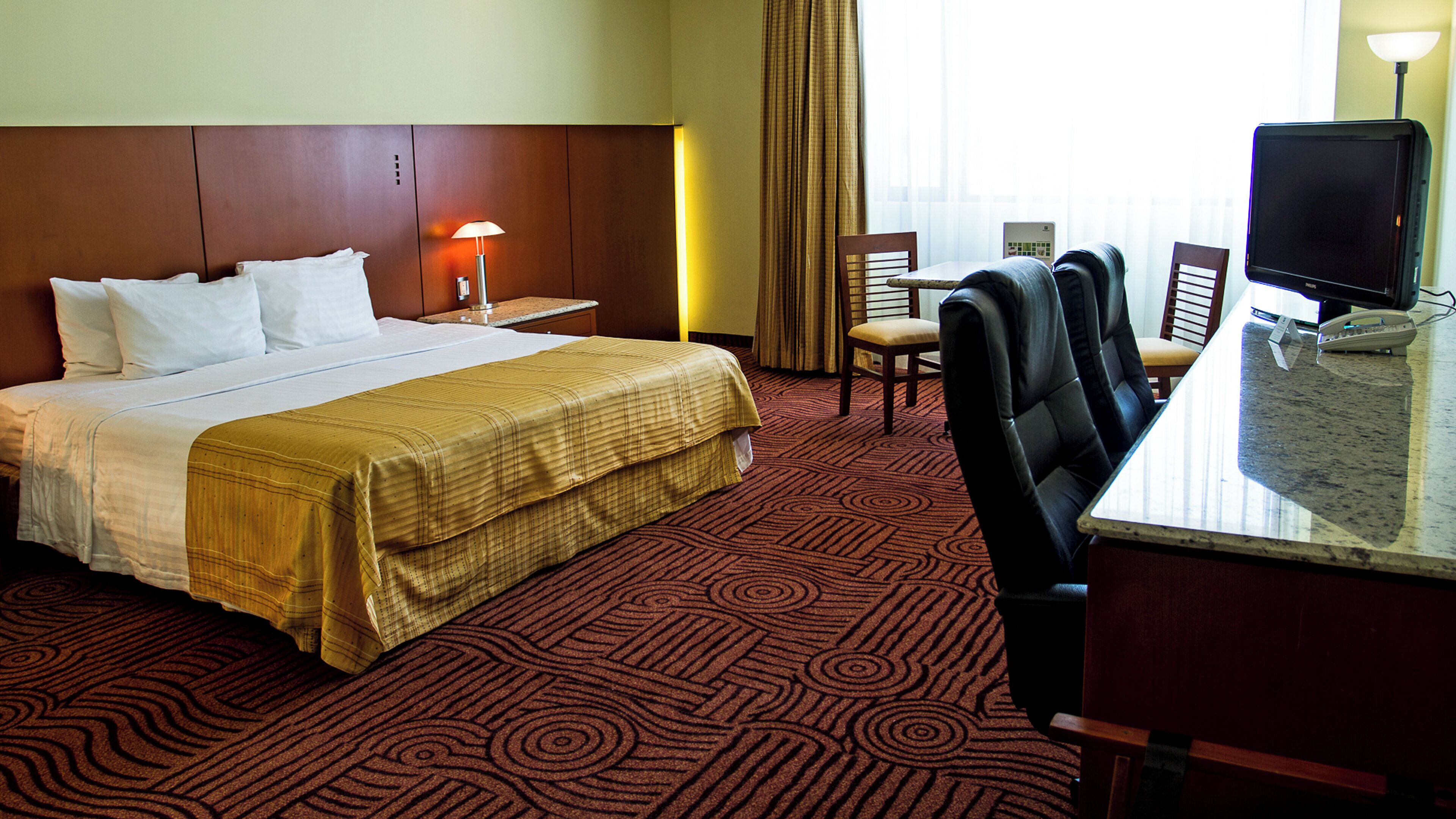 A hotel room with a bed, a desk with a computer, and a chair.