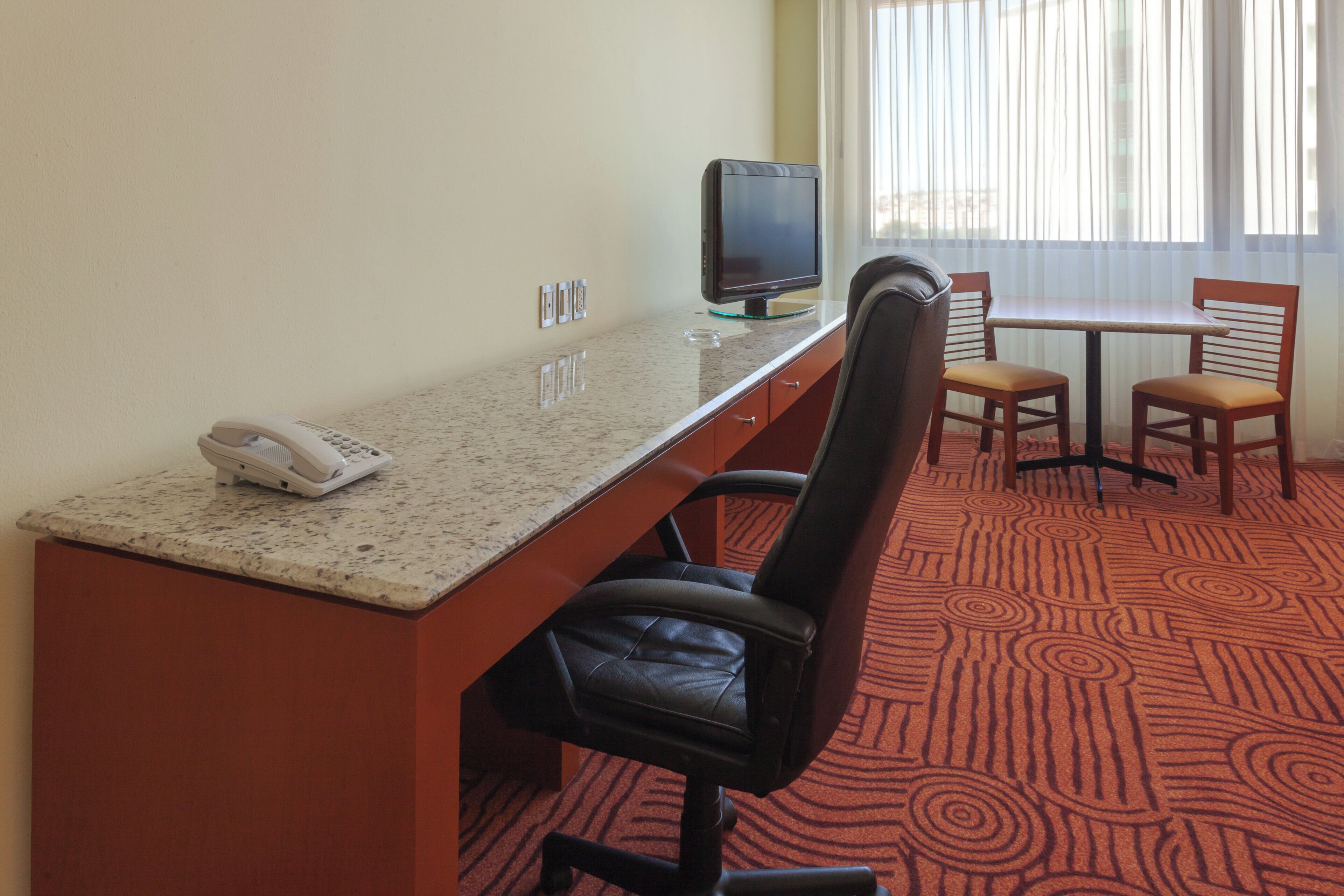 A hotel room with a desk, a chair, a television, and a telephone.