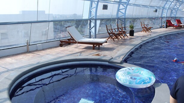 An indoor swimming pool with clear glass walls, lounge chairs, and a floating ring.