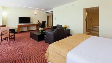 Una habitación de hotel con una cama grande, un escritorio con televisor de pantalla plana, dos sillones, una mesa de centro y una pequeña mesa con flores.