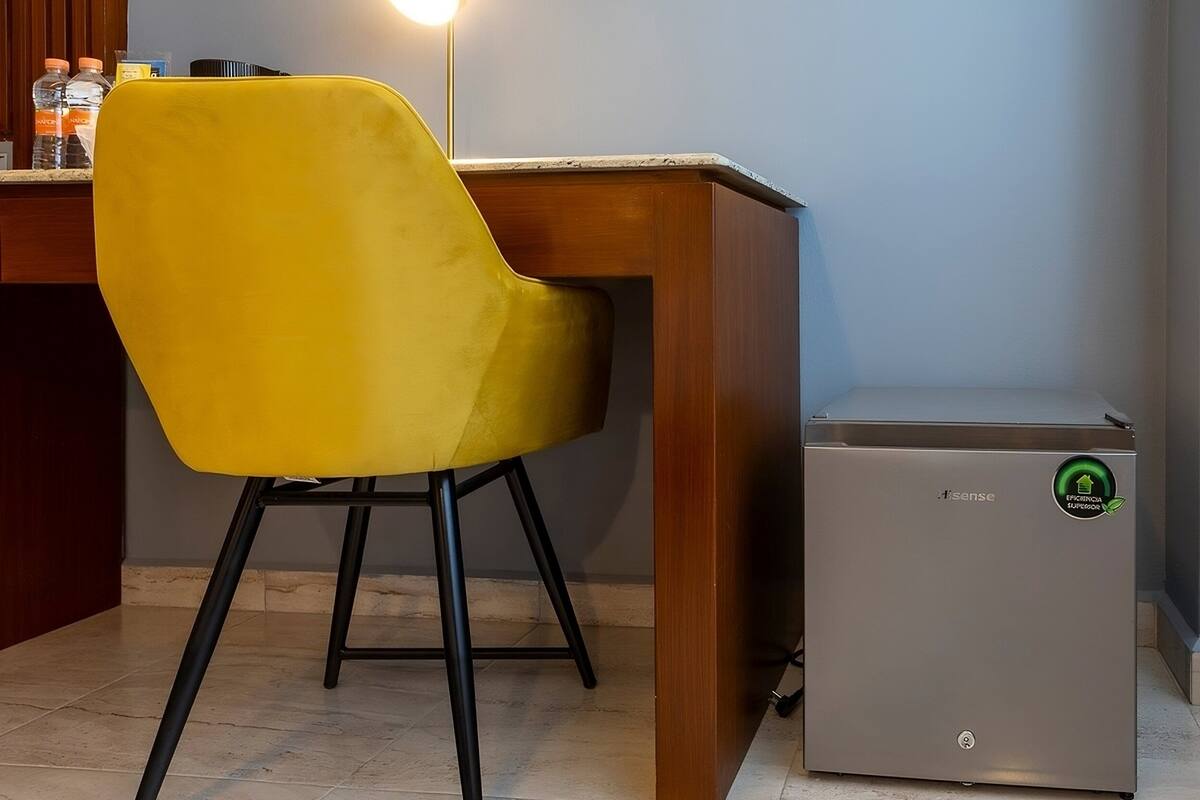 A yellow chair, a small grey appliance, and a wooden counter with bottles in the background.