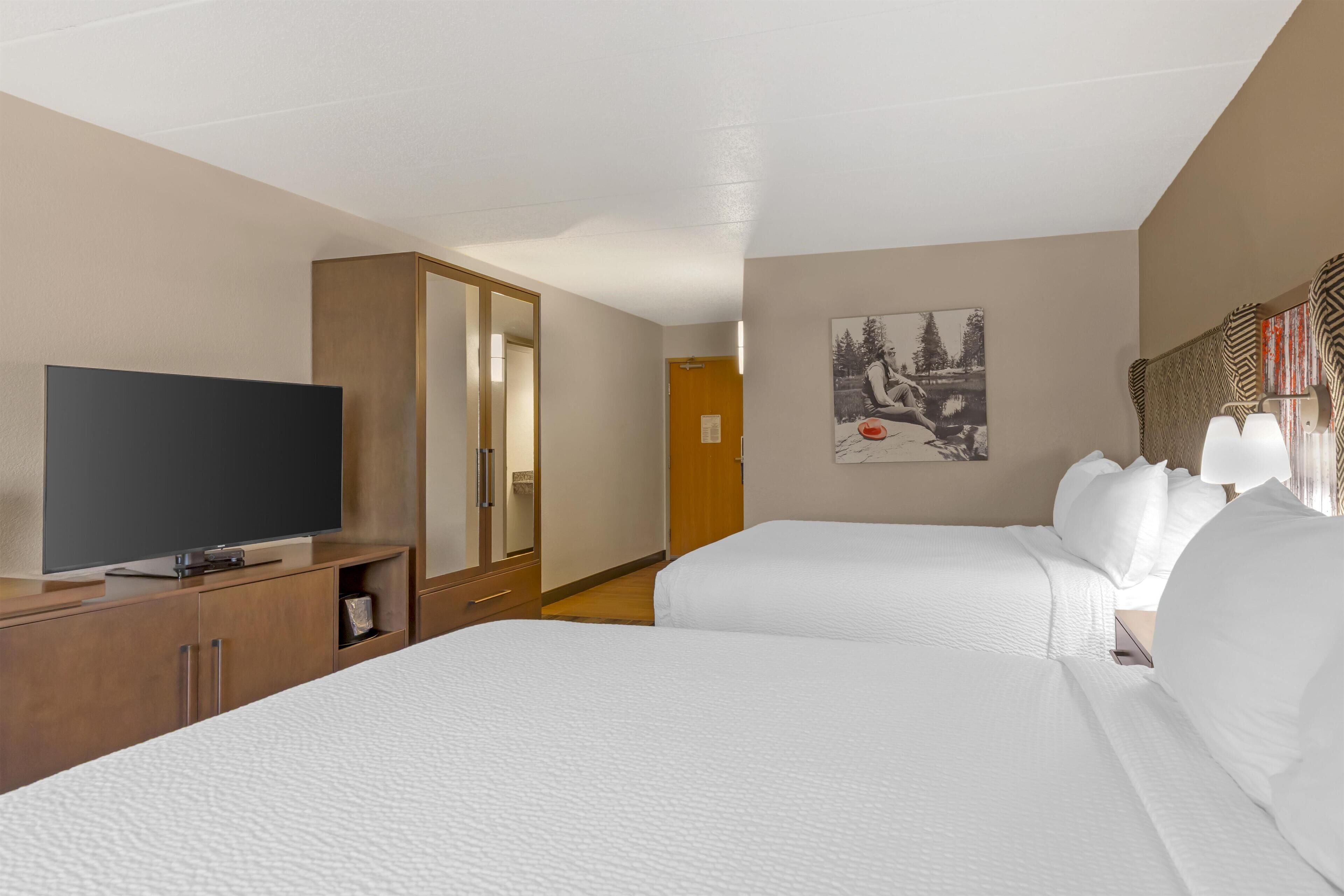 Une chambre d’hôtel avec deux lits, une télévision, une armoire et un tableau au mur.