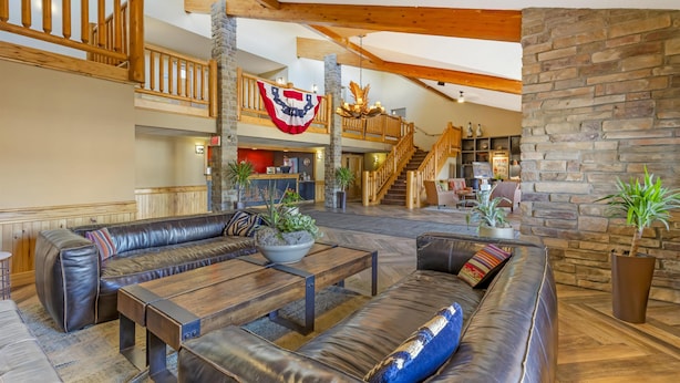 A spacious lobby with a high ceiling, wooden beams, a stone fireplace, and a staircase leading to an upper level. - Best Western Plus McCall Lodge & Suites (McCall)