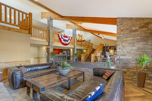 A spacious lobby with a high ceiling, wooden beams, a stone fireplace, and a staircase leading to an upper level. - Best Western Plus McCall Lodge & Suites (McCall)