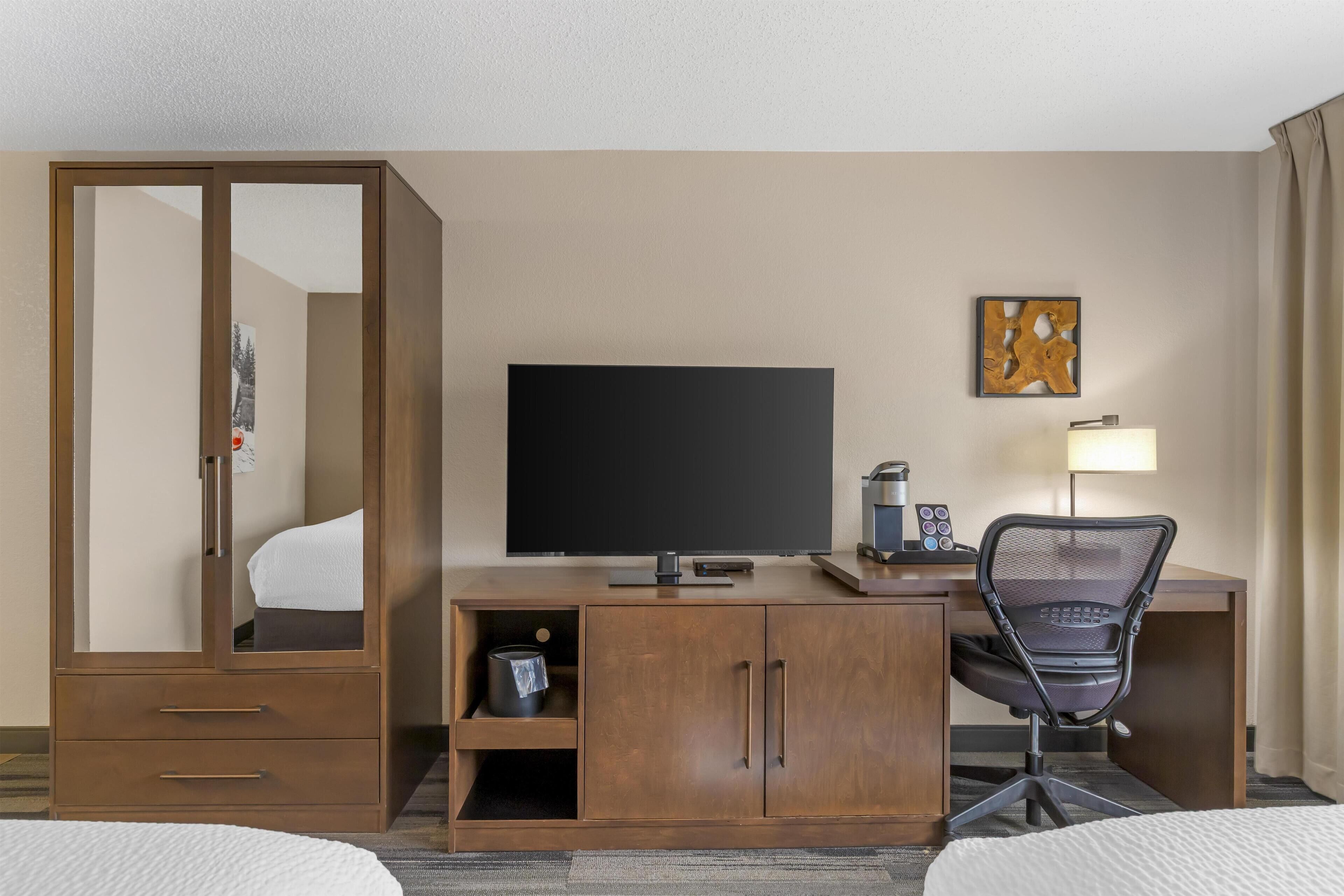 A hotel room with a wooden desk, a television, a chair, a bed, and a wardrobe.