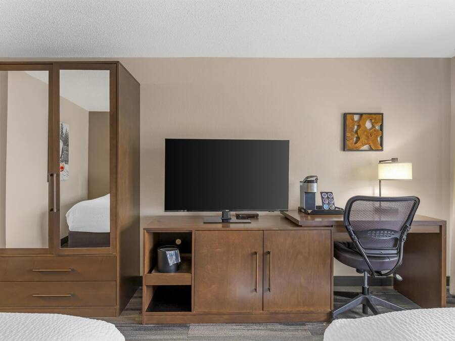 A hotel room with a wooden desk, a television, a chair, a bed, and a wardrobe.