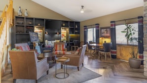 A spacious living room with leather sofas, a coffee table, and a fireplace. There are shelves with decorative items and a large window with curtains. - Best Western Plus McCall Lodge & Suites (McCall)
