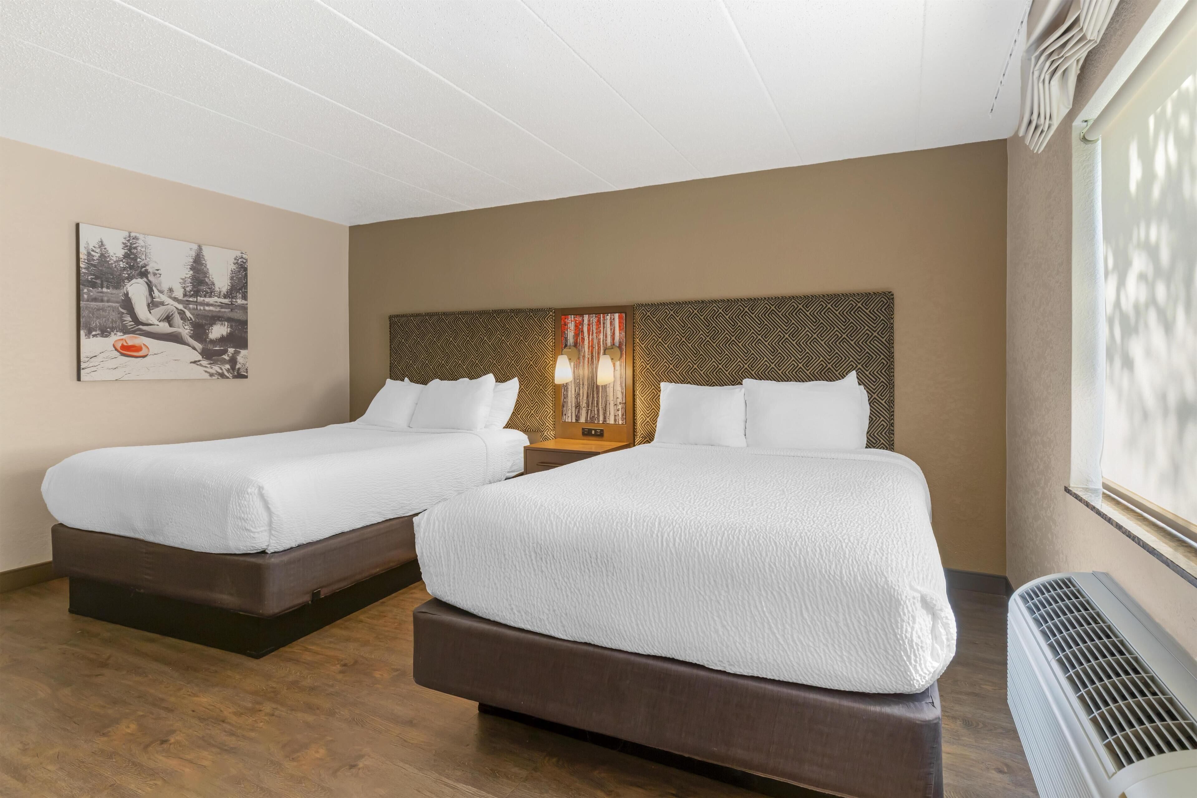 A hotel room with two beds, a large window, and a wall-mounted heater.