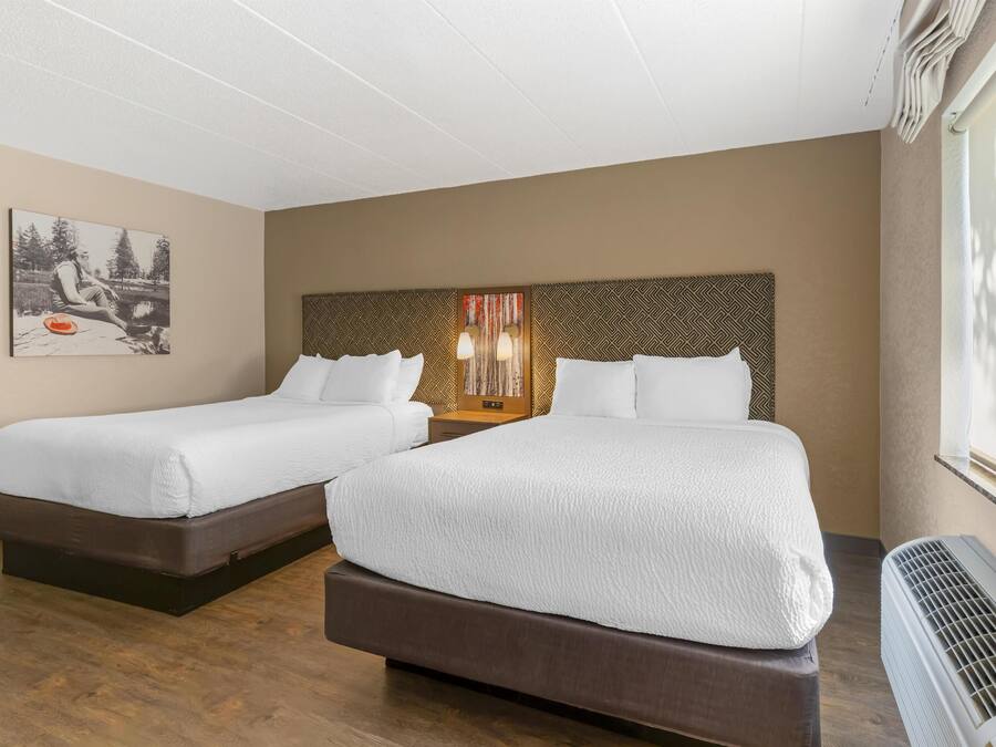 A hotel room with two beds, a large window, and a wall-mounted heater.