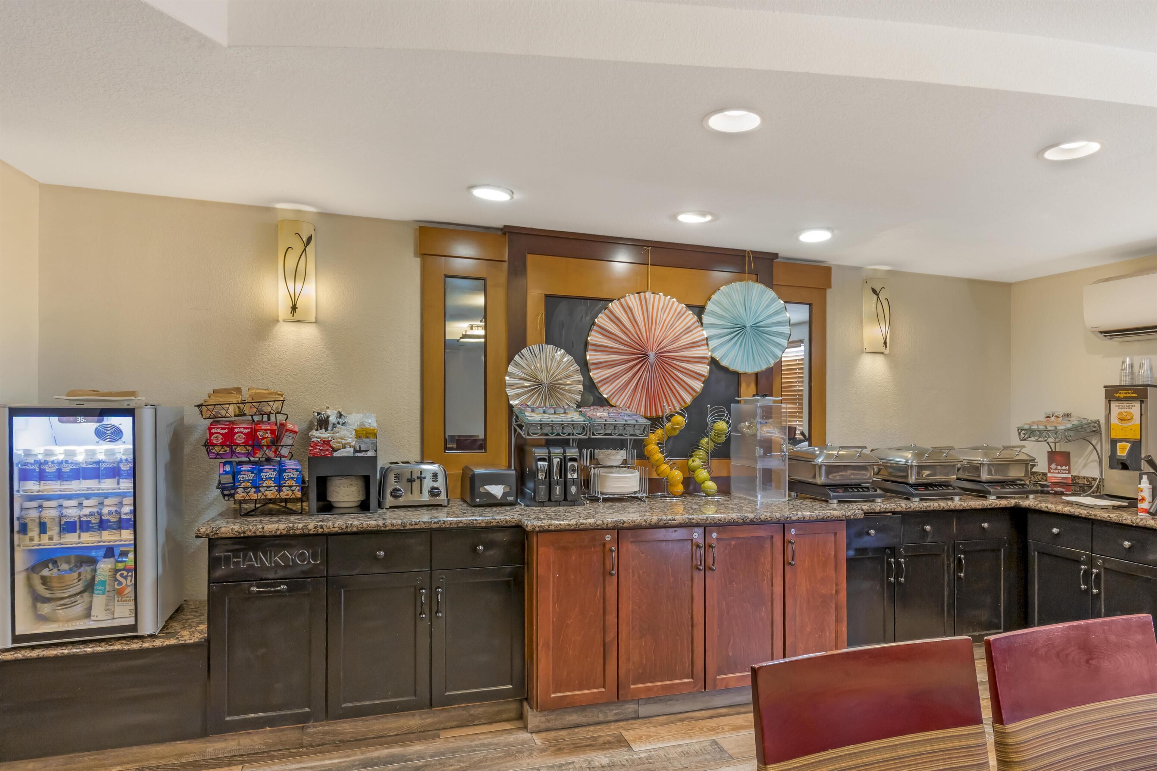 A kitchen with a refrigerator, coffee maker, and various kitchen appliances. There are wooden cabinets and a countertop with a sink.