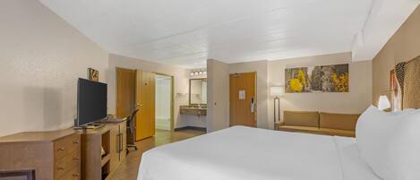 Habitación de hotel con una cama grande, un escritorio, una silla, un televisor y un baño visible a través de una puerta abierta.